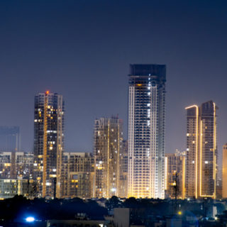 High rise multi story skyscrapers lit up at night with small houses in the foreground at night in gurgaon delhi